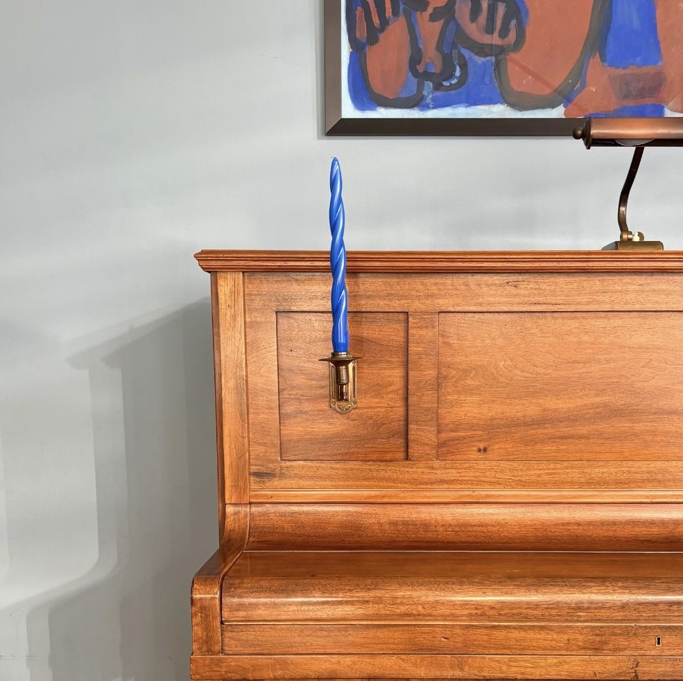 Ein Holzklavier mit einem blauen Kerzenhalter und modernem Kunstwerk im Hintergrund.