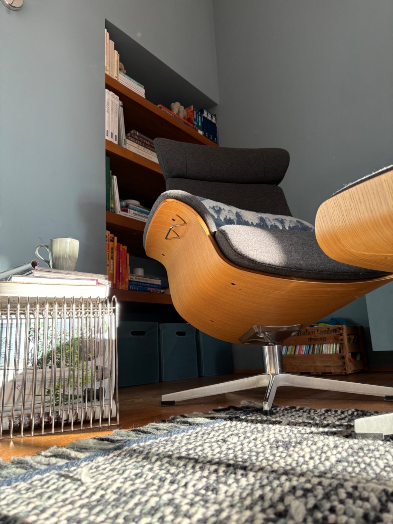 Moderner Sessel aus Holz mit Teppich und Bücherregal im Hintergrund.