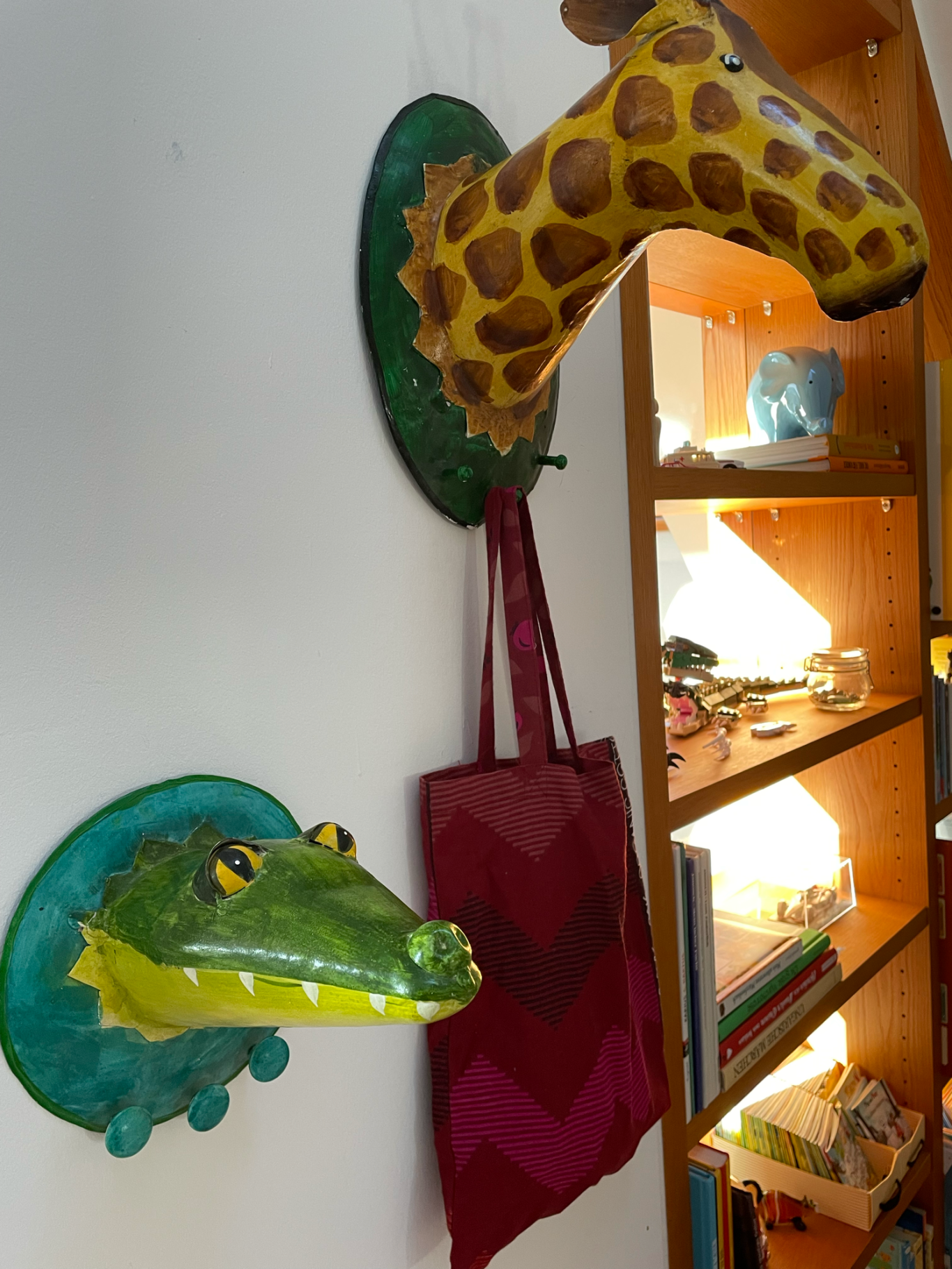 Giraffen- und Krokodilskopf-Dekoration an einer Wand mit einer Tasche darunter.