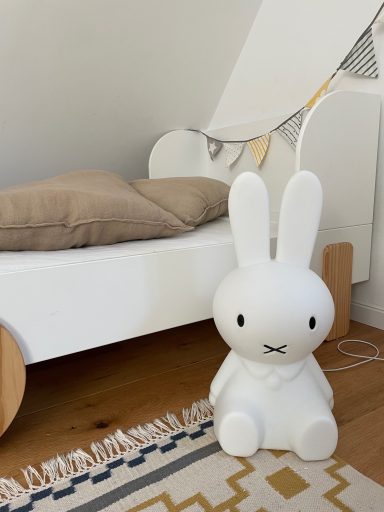 Weißer Hasenfiguren-Lampe steht neben einem Bett mit einem beige Kissen.