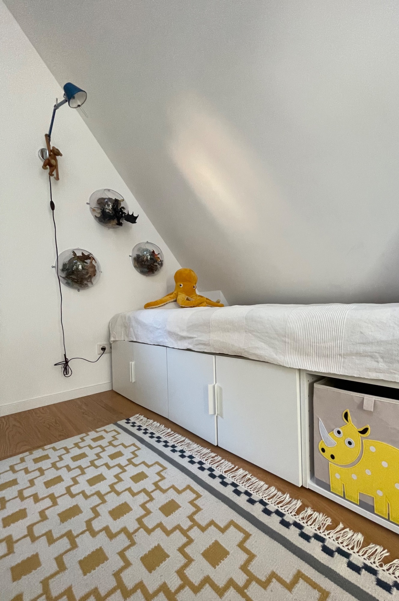 Gemütliches Kinderzimmer mit weißem Bett, gelber Dekoration und spielerischem Teppich.